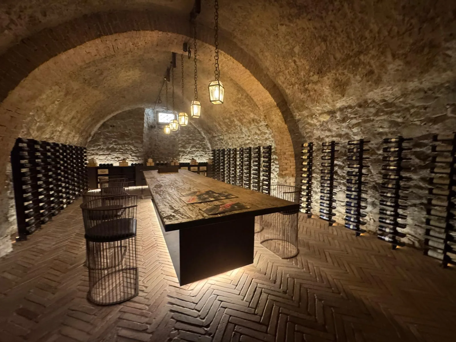 Sala di degustazione in una cantina toscana, con volta in mattoni, lanterne sospese e pareti di bottiglie