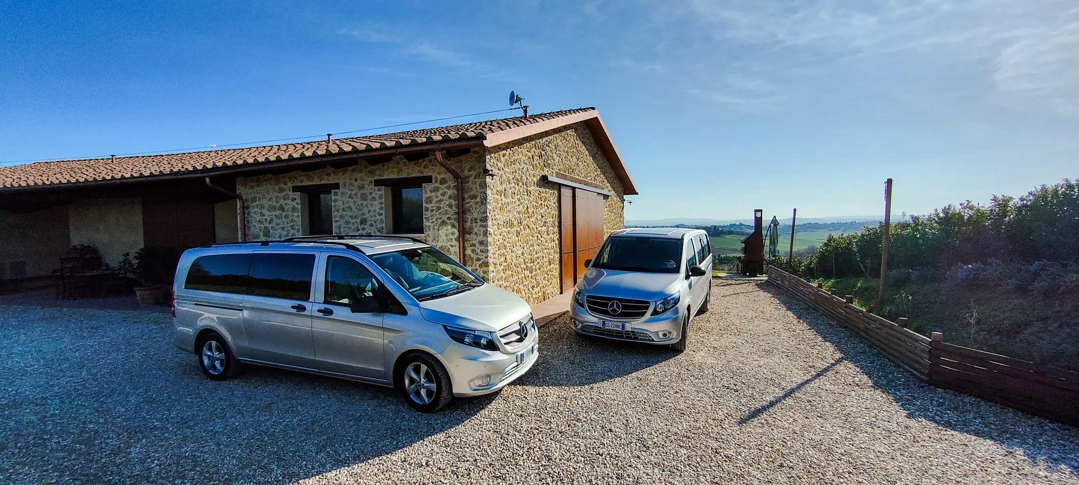 Due van Mercedes Vito grigi parcheggiati davanti a un casale in pietra, con le colline senesi sullo sfondo