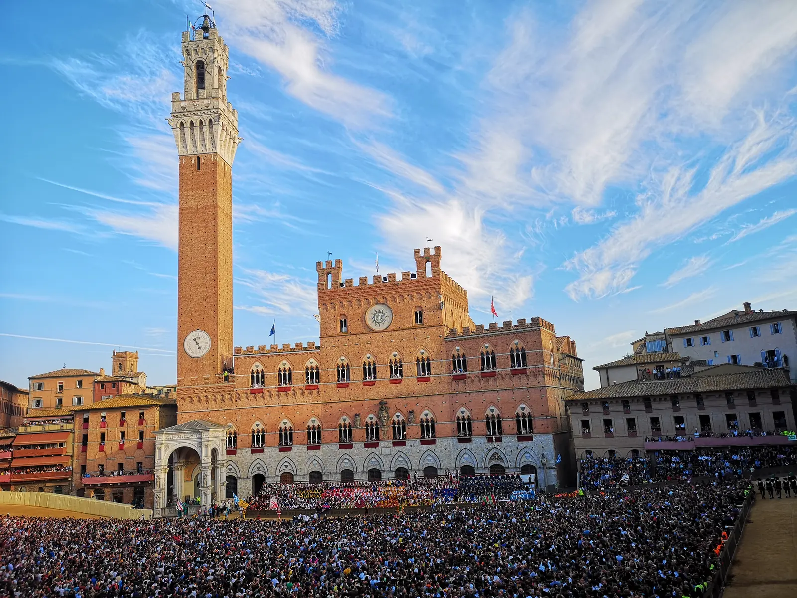 Piazza del Campo a Siena gremita di pubblico durante il Palio, con la Torre del Mangia e il Palazzo Pubblico